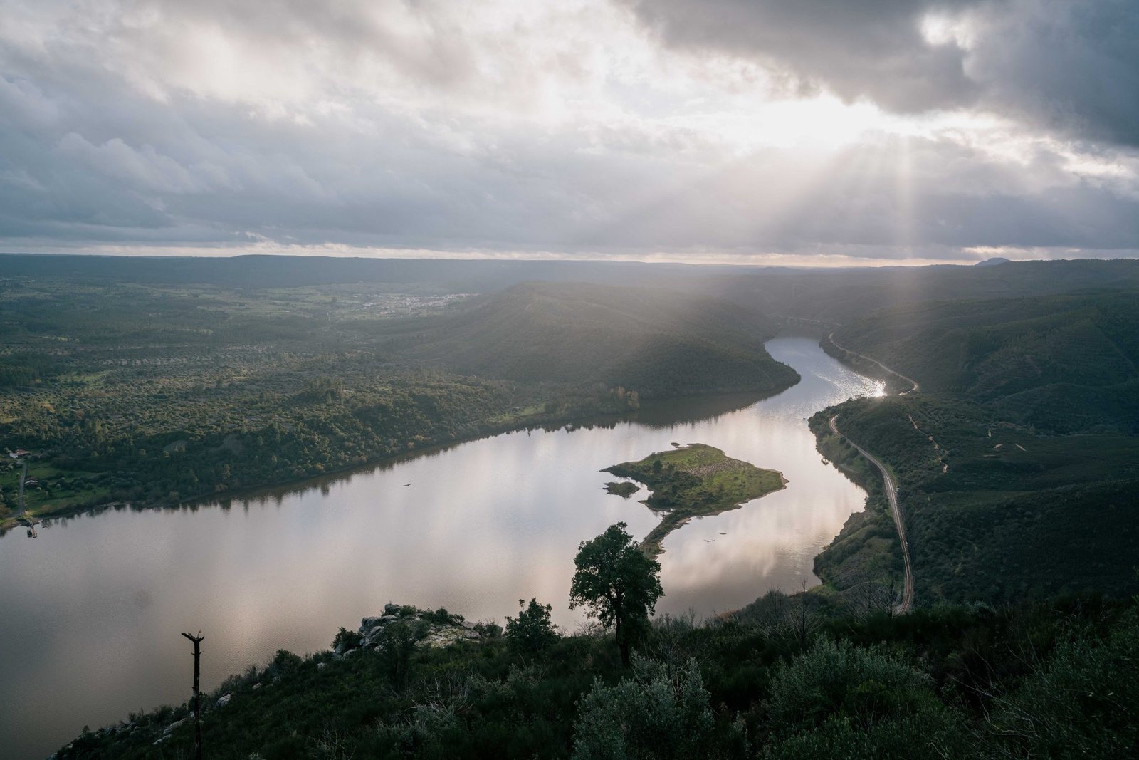 A panoramic view over a wide river flowing through a valley with a small island in the middle of it.