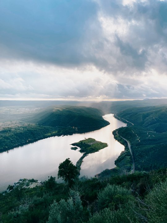 A panoramic view over a wide river flowing through a valley with a small island in the middle of it.