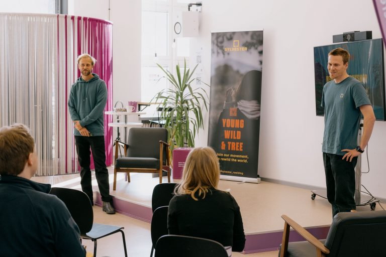 Two young men standing in front of a group, talking to the audience.