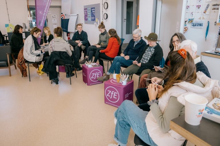 A group of people sitting together in small groups, talking to each other.