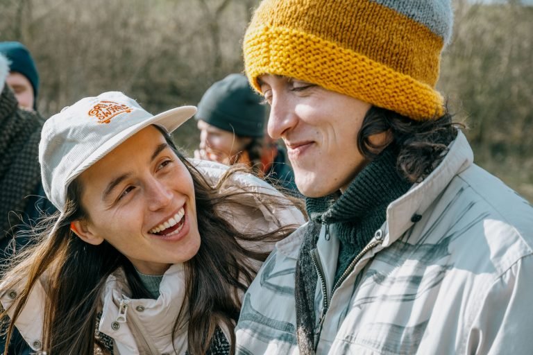 A young woman smiling at a young man - outdoors and in the sun.