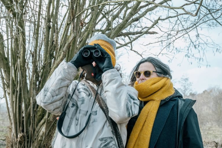 A man holding binoculars in front is eyes and a woman next to him.