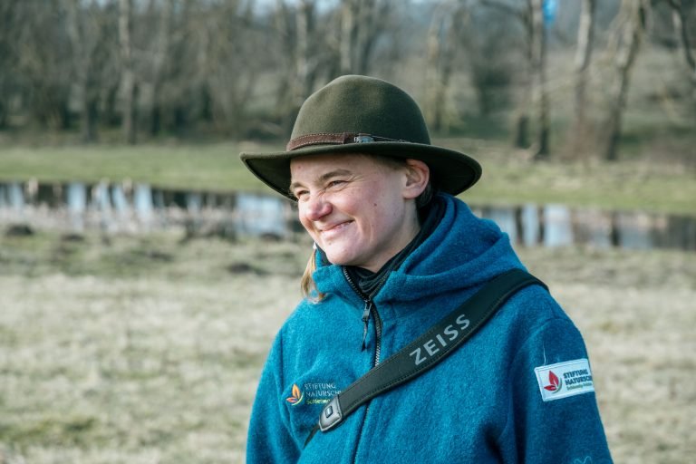 A young woman with a green hat smiling in the sun.