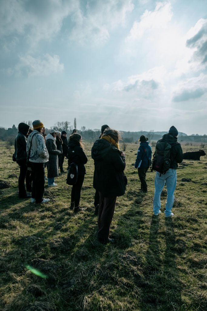 A group of young people standing on a pasture with cattle in he background.