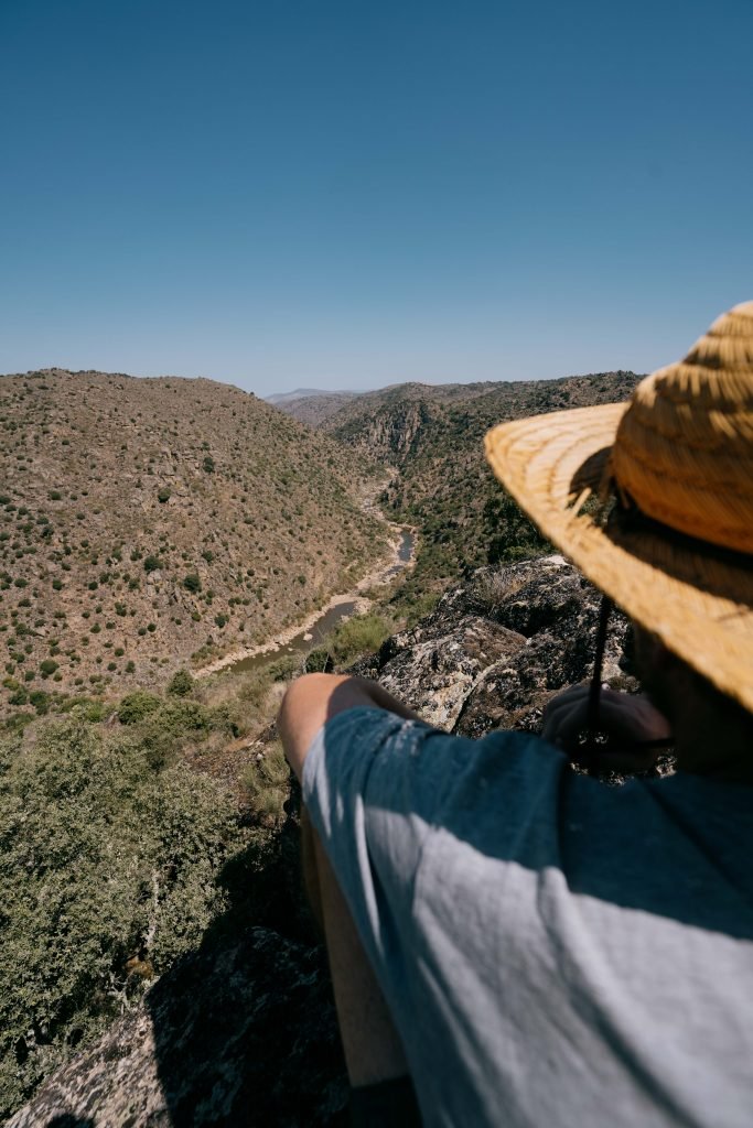 Man with a straw hat, sitting on top of a hill looking down into a vally