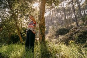 A young woman stands in a forest holding a piece of cork into the camera.