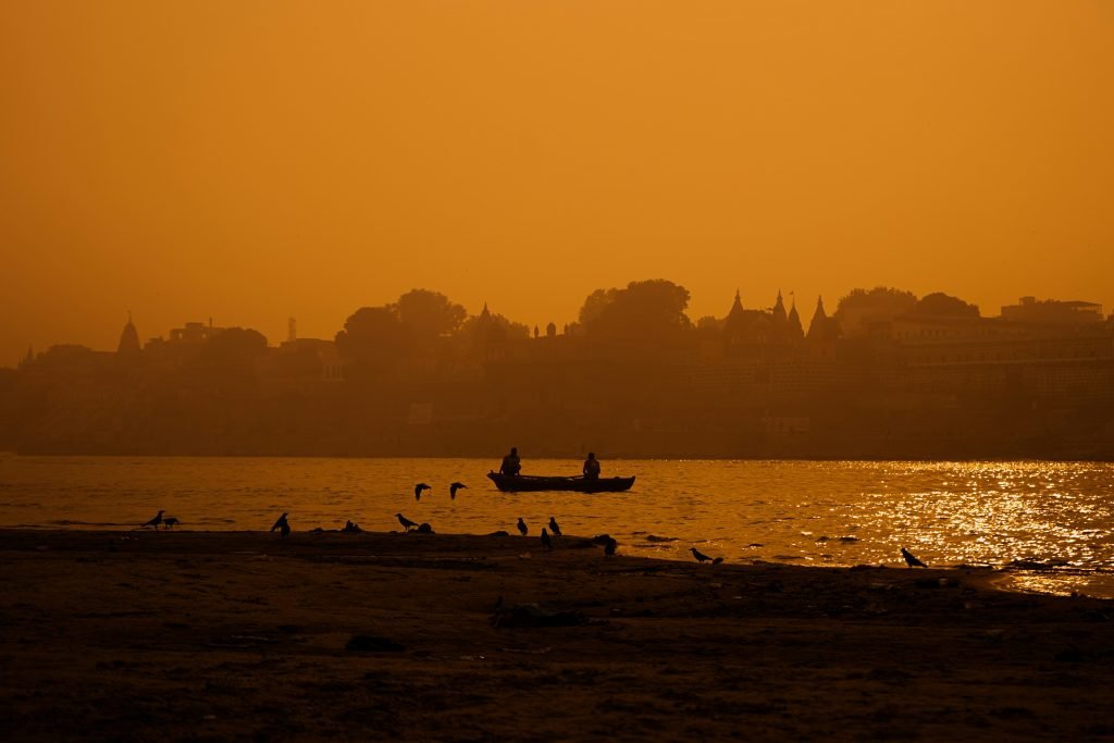A dusty red river with a fishing boat in front of a dusty skyline.