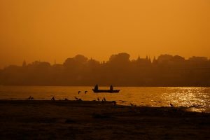 A dusty red river with a fishing boat in front of a dusty skyline.