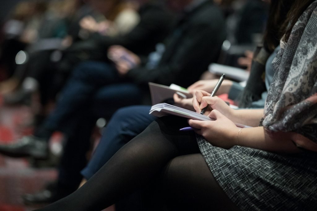 Several people sitting in a row taking notes.